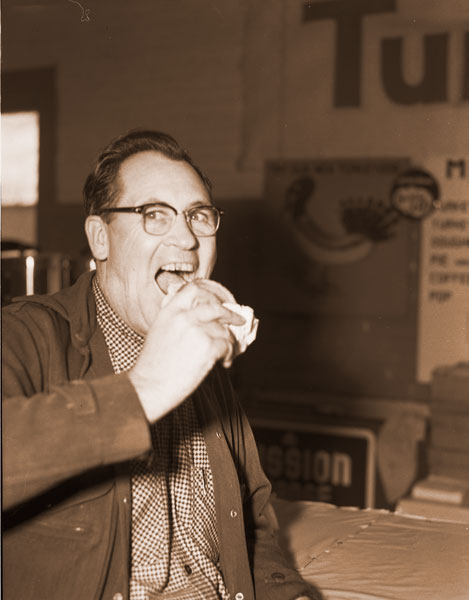 ##(Dec. 7, 1955) Dan O. Smith, McMinnville turkeyman, wouldn&rsquo;t be content with an ordinary hamburger at the Pacific Coast Turkey Exhibit. He goes for turkeyburgers at 20-30 Club booth. Booth also features turkeydogs for the first time this year.