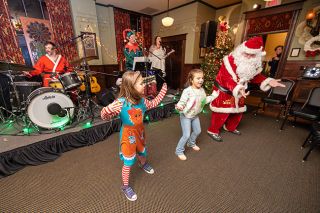 Rachel Thompson/News-Register##
Charlie DeRosso, 7, left, and Jaliyah Glaze, 8, dance alongside Santa Claus as Falcon Heart performs during a holiday benefit bash on Friday in Mattie&rsquo;s Room at McMenamins Hotel Oregon. Bandmembers Aaron DeRosso on drums, Marcus Glaze on keyboard and Jean Mastaler on electric violin hosted the family-friendly concert to support local food assistance through a food drive and raffle benefiting Yamhill Community Action Partnership and Saturday Morning Breakfast in Mac.