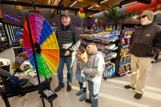 Rachel Thompson/News-Register##Anthony Dinsmore spins a prize wheel with his children, Grayson, 7, and Piper, 4, as Tom Baker looks on during the grand opening of the 7 Star Convenience Store in Carlton. The store sells snacks, groceries, produce and numerous beverages, along with &ldquo;Krispy Krunchy Chicken.&rdquo;
