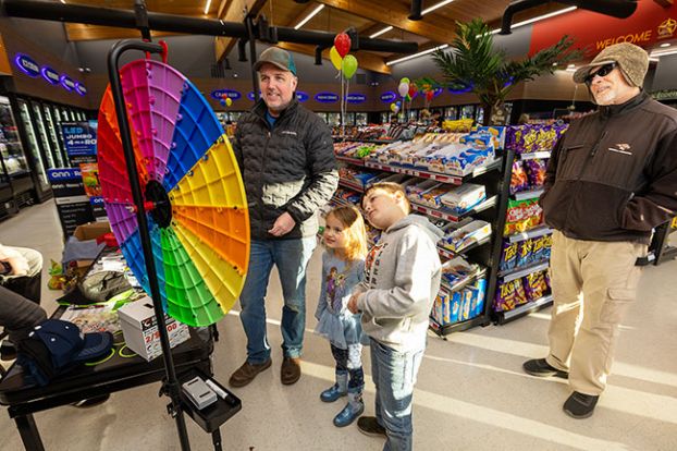 Rachel Thompson/News-Register##Anthony Dinsmore spins a prize wheel with his children, Grayson, 7, and Piper, 4, as Tom Baker looks on during the grand opening of the 7 Star Convenience Store in Carlton. The store sells snacks, groceries, produce and numerous beverages, along with &ldquo;Krispy Krunchy Chicken.&rdquo;