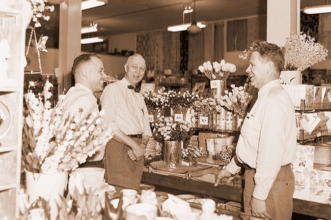 ##(Feb. 29, 1956) Name of Ramsey denotes three decades of variety store service to residents of McMinnville&rsquo;s shopping area. Preparing for celebration of the long business, son Bill Ramsey, left, and son-in-law John Good, right, pause to talk with L. F. Ramsey beside a display of Easter flowers.