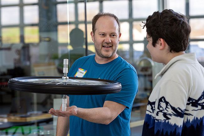 Rachel Thompson/News-Register##Volunteer Tristan Shell-Spurling spins a bicycle wheel used to demonstrate gyroscope physics and angular momentum for Liam Seibt, 13, of Salem.