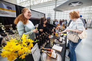 Rachel Thompson/News-Register##Beneath the wing of a vintage aircraft in Evergreen Aviation & Space Museum&rsquo;s Hercules Pavilion, Jessica Cortell, left, of Cortell Collection, chats with visitors Sunday during the McMinnville Wine & Food Classic. Joyce Campbell, center, pours a taste of Pinot Noir Blanc for Cynthia Rawlinson of Gaston. Cortell recently opened a tasting space in the historic 1928 Amity bank building, where the former vault has been transformed into a tasting room by reservation.