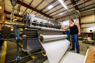 Rachel Thompson/News-Register##Tori Matheny, lead supervisor for the Imperial Fabrics bedspread department, checks a quilting machine stocked with rolls of fabric, batting (filling) and backing. The machine will cut all three layers into pieces of the right size, then quilted together to become bedding.
