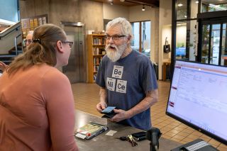 Rachel Thompson/News-Register##Earlier this year, Mike Paull of Amity speaks with librarian Teri Swanson at the McMinnville Public Library. The McMinnville Budget Committee committed funds for the library to reopen on Sundays next fiscal year.