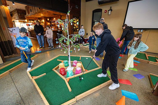 Rachel Thompson/News-Register##With school out this week, Conner Drorbaugh, 11, of McMinnville lines up a putt as his cousins Weston Owens, 9, of Amity, left, and Callynn, 7, right, take their turns at the Sweet Spot pop-up mini golf course inside the KAOS Building at Third and Galloway.