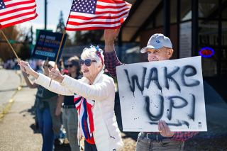 Rachel Thompson/News-Register##Kay Koudele of McMinnville, a resident at Hillside Senior Community, waves American flags outside Pacific Frame as her husband, Fred Koudele, holds a &ldquo;Wake Up!&rdquo; sign. Kay said relatives in Canada have asked why more Americans aren&rsquo;t speaking out. &ldquo;We&rsquo;re trying to do something,&rdquo; she said. Organizers of Saturday&rsquo;s No Kings rally assigned themes to a number of city blocks, including &ldquo;Red, White and Blue,&rdquo; &ldquo;Wild & Crazy&rdquo; and &ldquo;&rsquo;60s Peace.&rdquo;