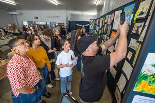 Rachel Thompson/News-Register##Amity sixth-grader Zaria Lugo beams as her father, Jesse, photographs her artwork during the Amity Daffodil Festival Saturday at the Amity Community Center. Zaria&rsquo;s piece, depicting two dragons framed by a wreath of daffodils and dandelions, earned a Judge&rsquo;s Choice award in the student art show. At left are her mother, Irene, and siblings Athena and Cyrus.
