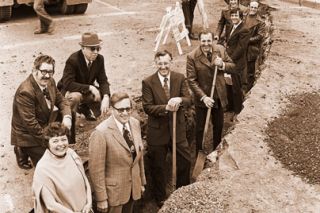 ##(April 6, 1976) Kizer Excavating began tearing up Third Street, making way for drainage system as initial work in downtown improvement for McMinnville. Project started Monday, after many months of work by Committee on Redevelopment and city staff. Pictured at right are most of the COR committee, standing in the first downtown ditch dug by Kizer. In the ditch are (I to r), Donna Jean McDaniel, Lee Perry, Glen Macy, Ernie Beckett, Chairman Bill Rutherford, Larry Wildman and Chamber Manager John Desmarteau. Behind them are Al Beeler, Jim Stanard and City Public Works Director Bill Blum (standing). Not pictured are COR members Phil Bladine, Wally Wright, Paul Durbin, Ish Duckett and Gale Johnson.