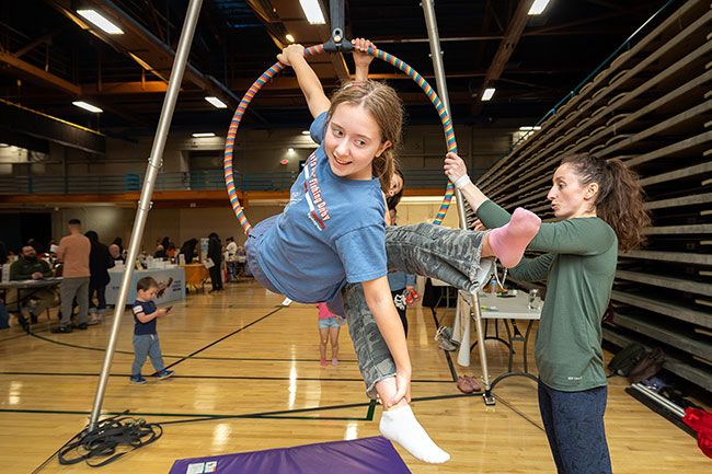 Rachel Thompson/News-Register##Samantha Reed and Eleanor Fair, both 11, share an aerial hoop as Savannah Stanton, right, a coach with Earth & Elevate, offers guidance during Community Wellness Day on Saturday, April 18, at the McMinnville Community Center. The free event, hosted by the SNACK Program and McMinnville Parks and Recreation, featured interactive booths, physical activities, games and an obstacle course.