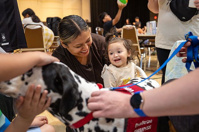 Rachel Thompson/News-Register##Ariana Corona Sanchez, 1 1/2, reaches toward Finn, a Dalmatian with Paws for Love Therapy Dogs, as her foster mother, Karen Diaz, smiles during Community Wellness Day on Saturday, April 18, at the McMinnville Community Center.