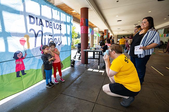 Rachel Thompson/News-Register##Sisters Victoria Ramirez, 4, and Madi, 5, pose in front of a &ldquo;D&iacute;a de los Ni&ntilde;os&rdquo; backdrop on Saturday, April 25, as Katie Noyd of McMinnville Parks and Recreation takes their picture, while their mother, Laura, looks on at right. Families received Polaroid prints to take home.