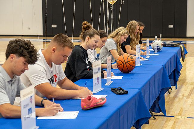 Nathan Ecker/News-Register##Trenton Ruston, Jaxson Howard, Alyssa McMullen, Lyliana Rideout, Haley Miersma, Eliza Nisly and Emma Northrop sign their letters of intent to play college sports during Amity&rsquo;s signing day in the Warrior gymnasium on Wednesday, May 13. Ruston and Howard still have track and field championships in their sights before graduation, while the group of girls went on to win a flag football tournament game two hours later.