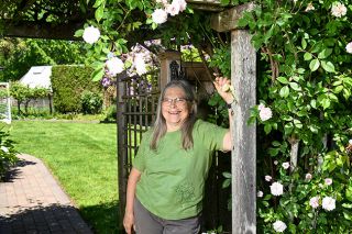 Rusty Rae/News-Register##Shelley Gowell stands beneath a pergola covered with C&eacute;cile Br&uuml;nner roses that marks the dividing line between her front and back yards. The front is a showplace of roses, rhodies, lilies, dahlias and annual blossoms; the back features a vegetable garden.