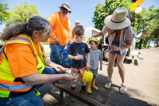 Rachel Thompson/News-Register##Sheridan Public Works Services Coordinator Sandy Davis, left, hands stickers to 5-year-old Aiden Laflen of Sheridan while 3-year-old Deveraux Driscoll of McMinnville stands nearby. Looking on are Deveraux&rsquo;s mother, Cheyenne Driscoll, right; sewer operator Jerad Gage-Brickeen, background left; and street maintenance worker Jake Thompson, background center. Children received free toy hard hats, safety vests, glasses, stickers and balloons from public works employees.