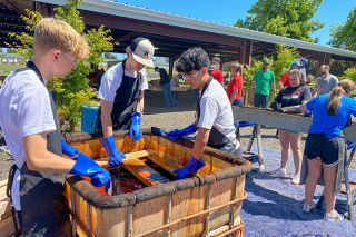 Starla Pointer/News-Register##From left, McMinnville High School students Hunter Gibbons, Colton Maxwell and Ryan Lai dip a newly built headboard into a vat of stain during the Sleep in Heavenly Peace bed build Sunday at the Yamhill County Fairgrounds. About 35 volunteers helped build bed frames for children who need restful places to sleep.