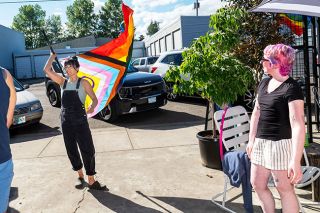 Rusty Rae/News-Register##Mac Market owner Diana Riggs twirls the Pride flag announcing the kickoff of Pride Month during festivities Thursday evening. At right is Haylee Goodpaster, a barista at Alea Bakery, who installed the flag on the market building a few moments later.