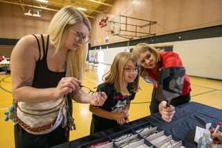 Rachel Thompson/News-Register##Emery Rivas, 8, looks at her reflection while choosing eyeglass frames with help from her mother, Kayla Lambert, left, and optometry student Katrina Billinton during a free eye clinic Friday, June 5, at Faulconer-Chapman School in Sheridan. After trying several options, Emery chose the pair in Lambert&rsquo;s hands. About 40 Sheridan students will receive prescription glasses through the clinic next month.