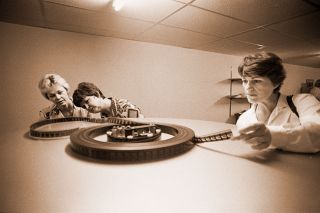 ##(June 12, 1981) The Mac Tri-Cinema opens its doors to the public at 6 p.m. today, with shows starting a half-hour later. Tours of the facility on north Highway 99W were given during a reception Thursday. Examining a reel of film are Sharon Amundson, Gaynelle Henderson and Ursula Doud. Two full-length movies can be held on each reel, eliminating the need to switch reels during a film, according to theater Manager Greg Kohler. If the film breaks, the projector automatically shuts down, the auditorium lights go on, the intermission music starts and employees in the snack bar are alerted to the problem by a warning light. The theater has three 200-seat auditoriums.