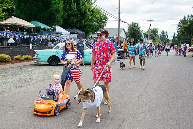 Ossie Bladine/News-Register##Jenny Zook pushes Sadie, 3, in a U.S.A. decorated toy car in the Lafayette kids parade, with Jeremy Zook and dog Ollie walking alongside.
