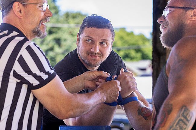 Rachel Thompson/News-Register##Referee Mark Owen, left, prepares Vakhtang Beridze of Vancouver, Washington, and event organizer Nicolas Mode of Amity for a match during an arm wrestling tournament at Garden Spot Park in Willamina. The competition was part of Willamina&rsquo;s annual Old Fashioned Fourth of July festival, which also featured a logging show, car show, food and fireworks.