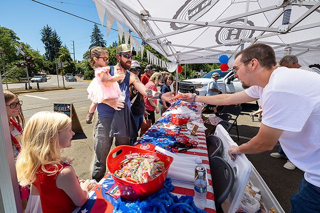 Rachel Thompson/News-Register##Collin Whitmore, a Hampton Lumber employee, right, hands an ice cream treat to Tyler Nicholson of Willamina and his daughter, Haven, 3, Saturday in Willamina. Hampton Lumber&rsquo;s booth in the Coyote Joe&rsquo;s parking lot handed out free ice cream, popsicles and bottled water to visitors.