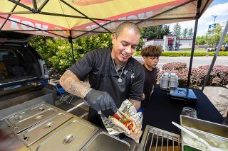 Rachel Thompson/News-Register##Amador Hernandez adds jalape&ntilde;os as he serves up a Jefe Dog, one of the specialties at his new El Jefe&rsquo;s Dogs food stand, located in the Lowe&rsquo;s parking lot. Open 10 a.m. to 6 p.m. Tuesday through Saturday, the stand serves other hot dog specials, chips and beverages. At right, Karmelo Hernandez, 12, helps his dad run the stand.