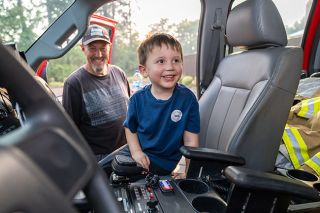 Rachel Thompson/News-Register##Bear Vinton, 3, of Dayton flashes a wide grin from the front seat of a fire truck after sounding the siren. His grandfather, Larry Wood, watches with a smile.